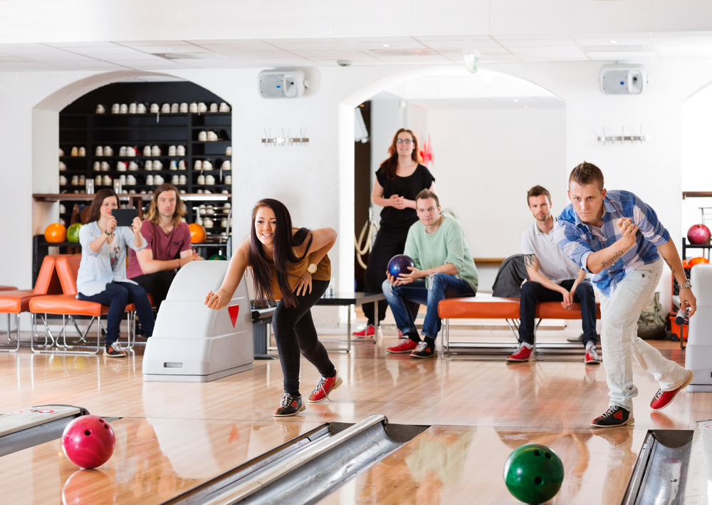 People sitting on couches watching people bowling at their lanes.