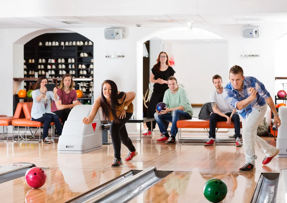 People sitting on couches watching people bowling at their lanes.