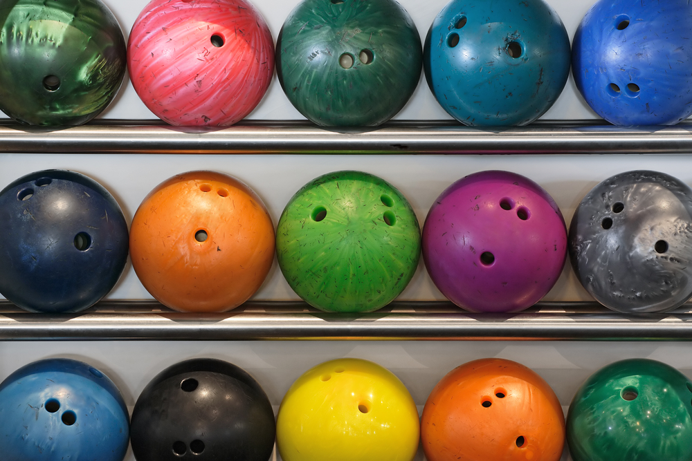 Mulitple old, dented, and chipped bowling balls on a metal rack that someone will need to figure out what to do with old bowling balls