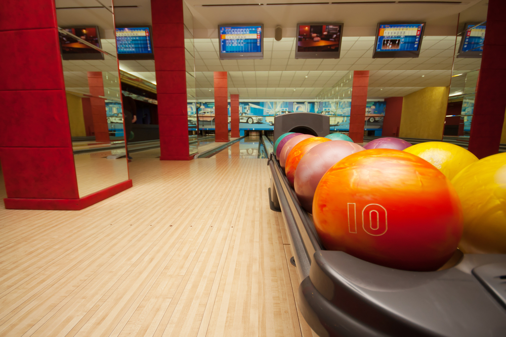 The inside of a bowling alley with vibrant red colors and mirrors on the walls. The ball return has several bowling balls on it in many different colors. The wood floors are shiny.
