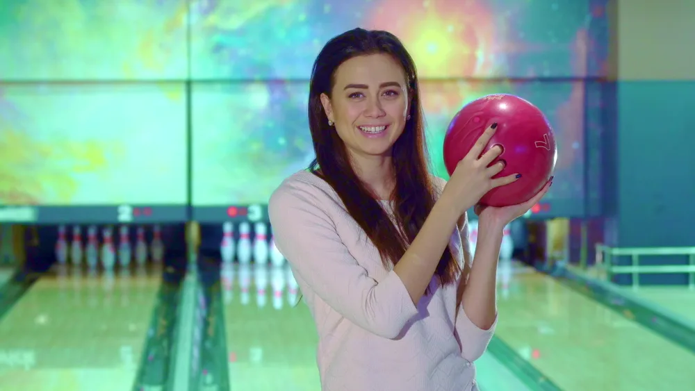 This image shows a woman league bowler holding a bowling ball and smiling.