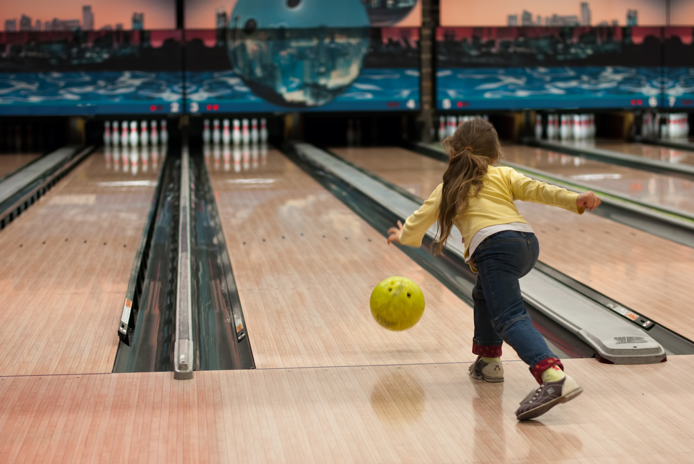 Young girl playing in a bowling alley. The average bowling scores for each age group vary. For bowling less than 10, it's 20 to 70 points.