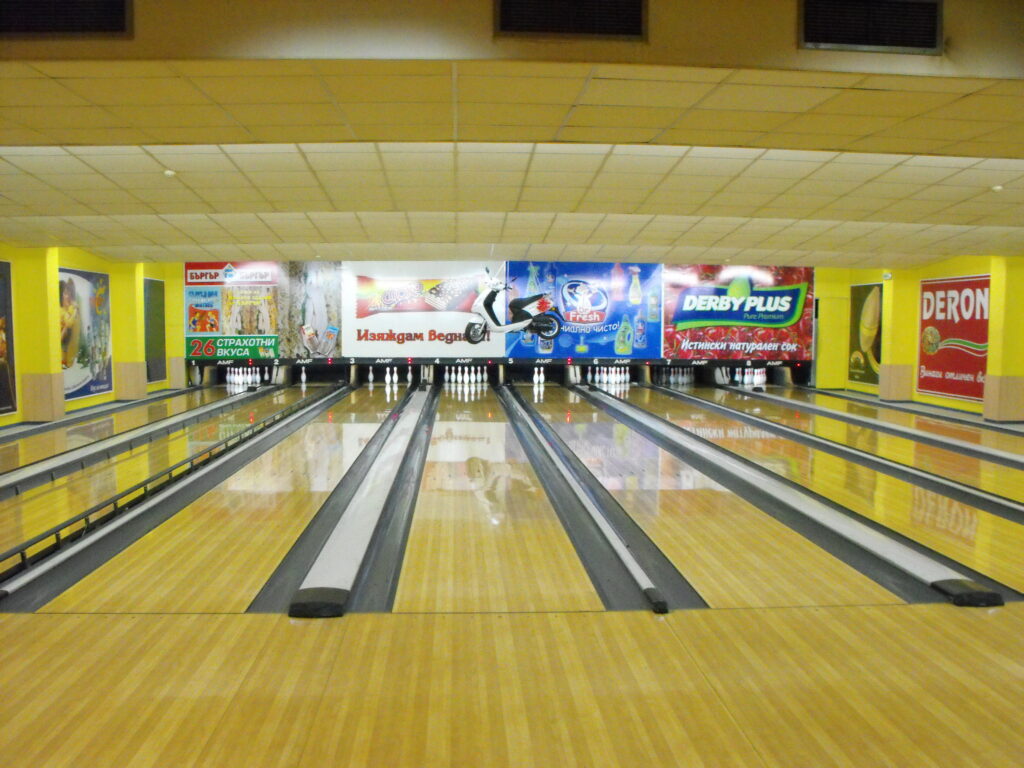 Eight bowling lanes and one with bowling bumpers extended, displaying a glossed lane surface and oil patterns. The foul line is visible on three of the lanes.