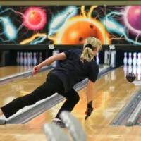 A lady that plays in two bowling leagues rolling a strike after using a ball cleaner for proper maintenance.