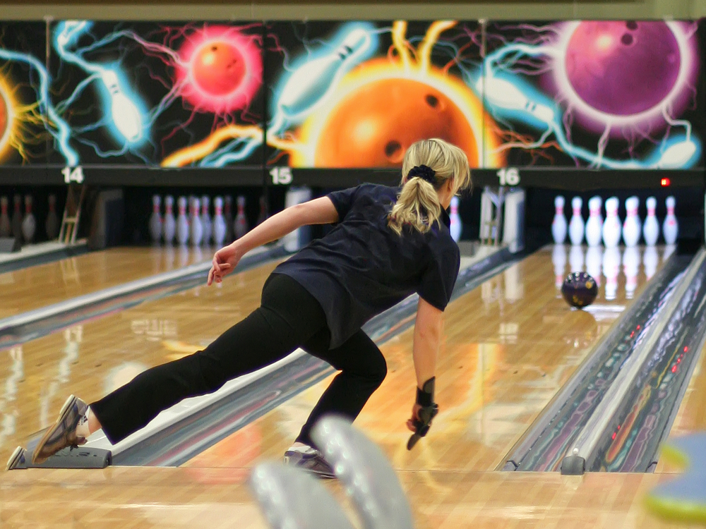 A lady that plays in two bowling leagues rolling a strike after using a ball cleaner for proper maintenance.