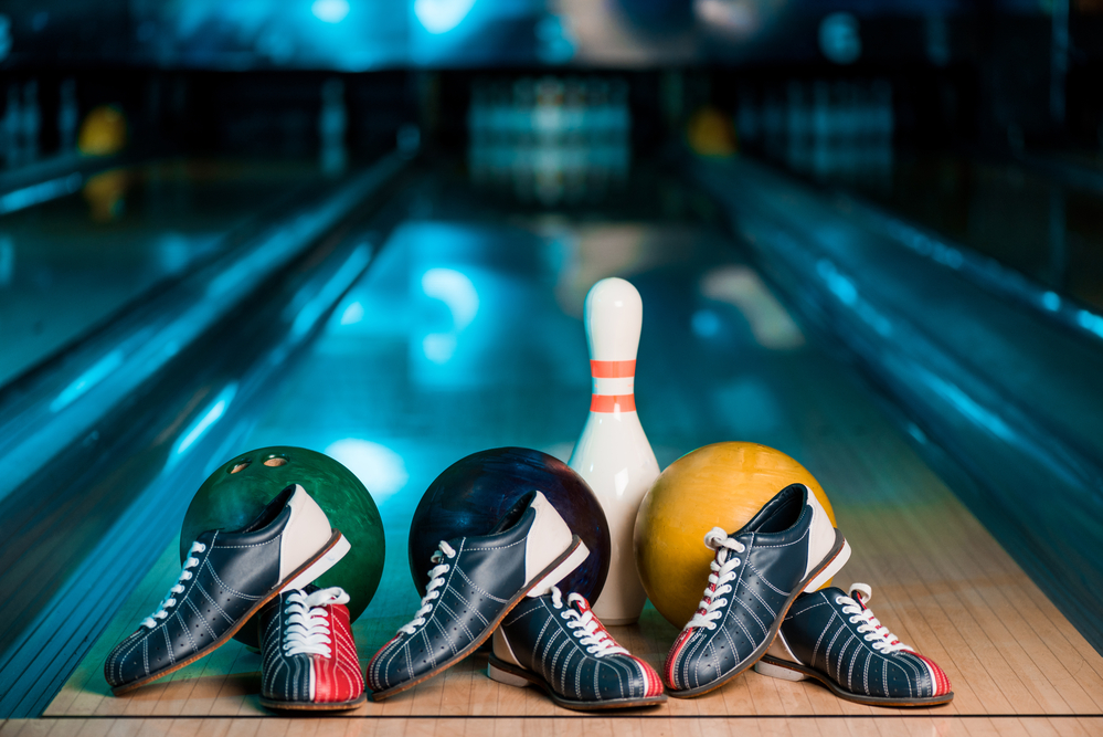 Three different bowling balls, green, blue, and yellow, and three pairs of tri-colored bowling shoes, red, white, and blue, are top performers equipment.