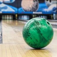 Close-up of green bowling ball against background of empty lanes in bowling alley. Active leisure. Sports activities for whole family. Space for text.