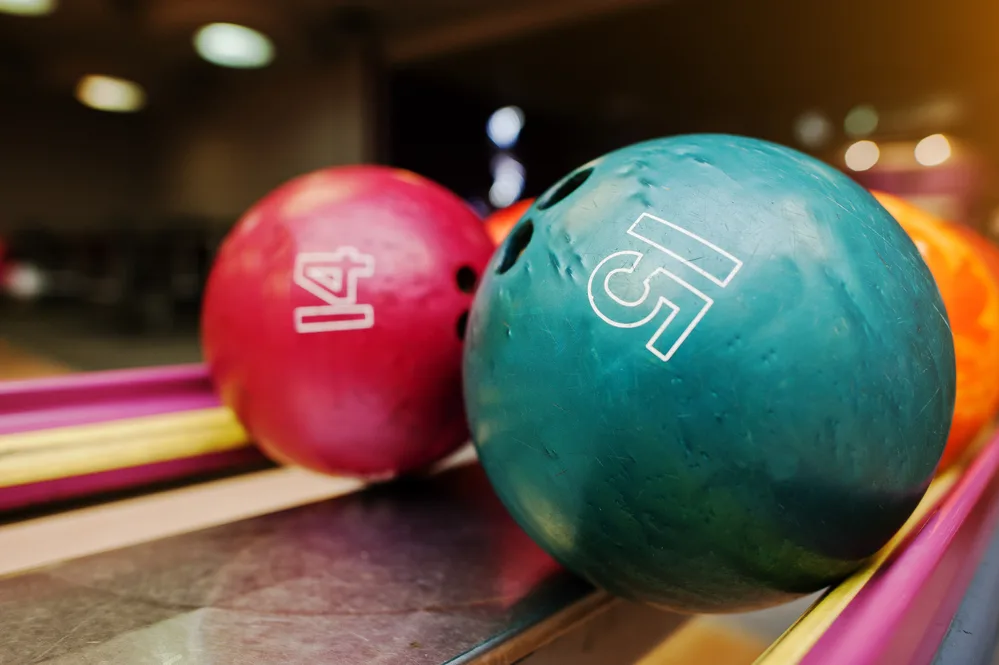 14 and 15-pound drilled bowling balls sitting on a ball return after being used by a family of amateur bowlers.