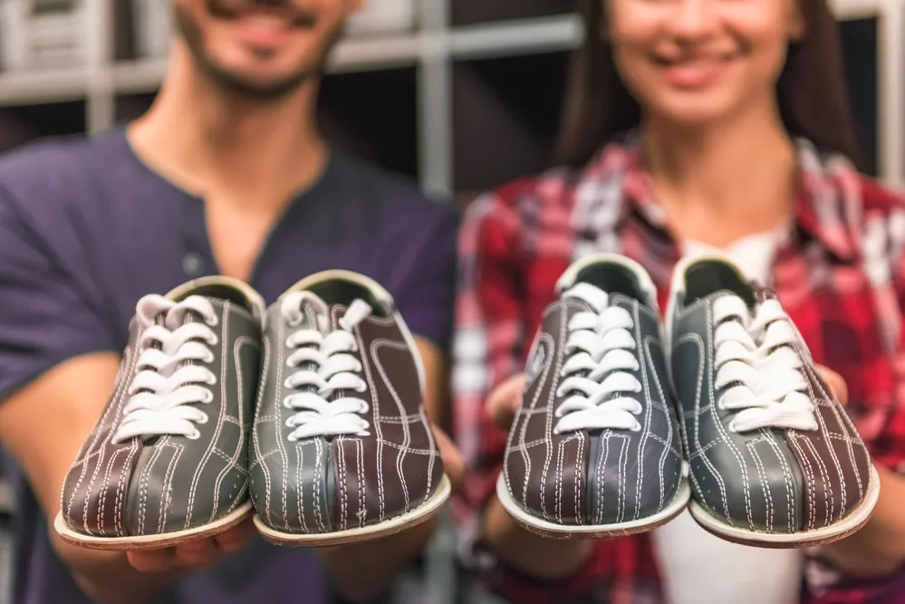 Cropped image of cheerful young couple holding bowling shoes and smiling because wearing street shoes or athletic shoes are prohibited.