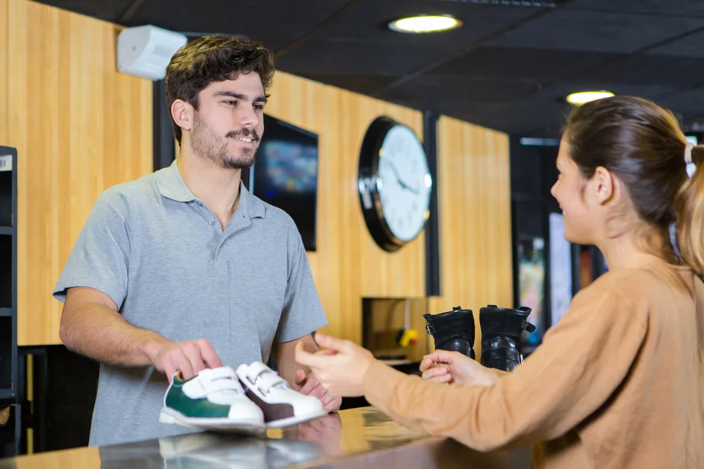 A lady getting shoes at the counter as she prepares for a few games of bowling practice on a wooden bowling lane.