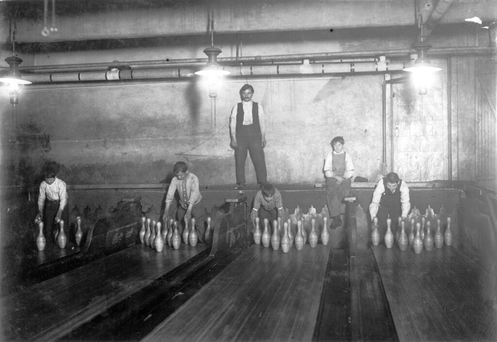 Four possible wood lanes and four young boys' jobs are to reset fallen pins after each bowler.