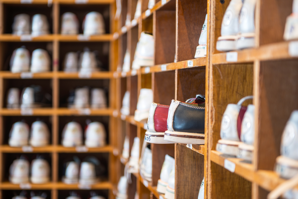 A shelf full of the same size bowling shoes store at the bowling alley right next to a stand of house bowling balls.