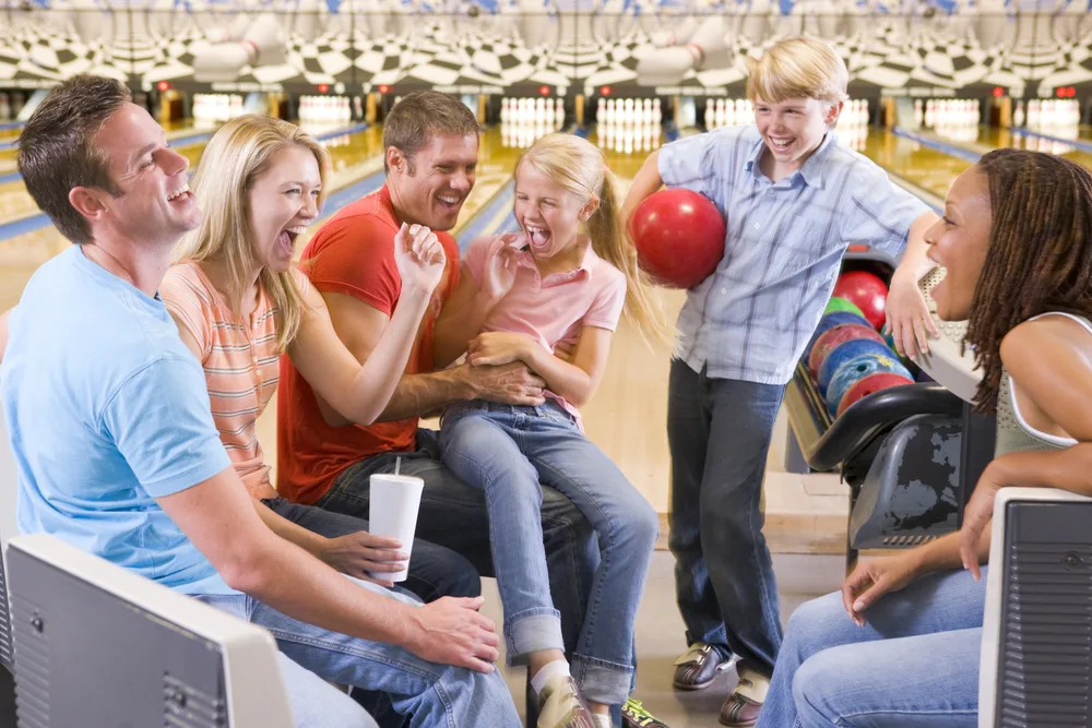 A family bowling fun night where dad has on a light blue t-shirt in a cosmic environment – common in bowling centers.