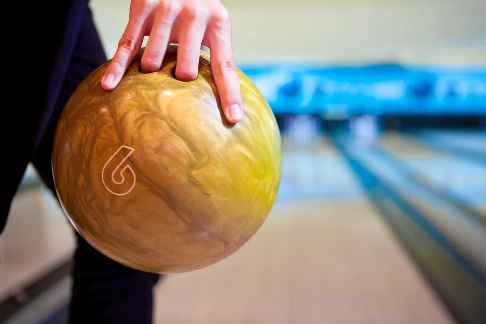 A man holding a 6-pound bowling ball as he prepares for a game of bowling with family and friends.