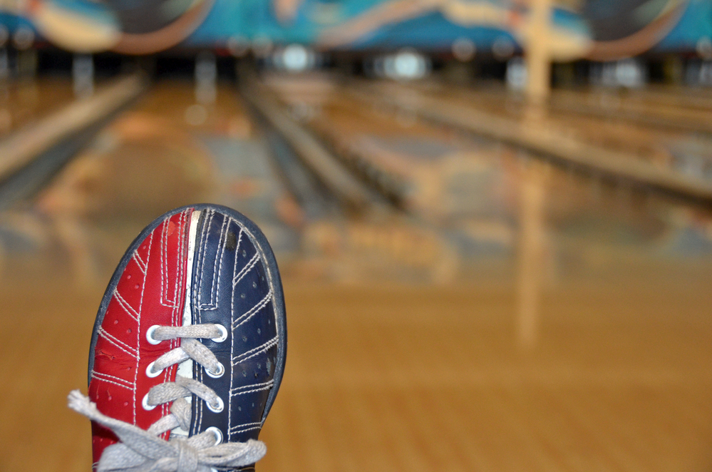 A red and blue bowling shoe on a blurred background of a bowling alley, will be cleaned with a soft cloth to avoid leather flaking.