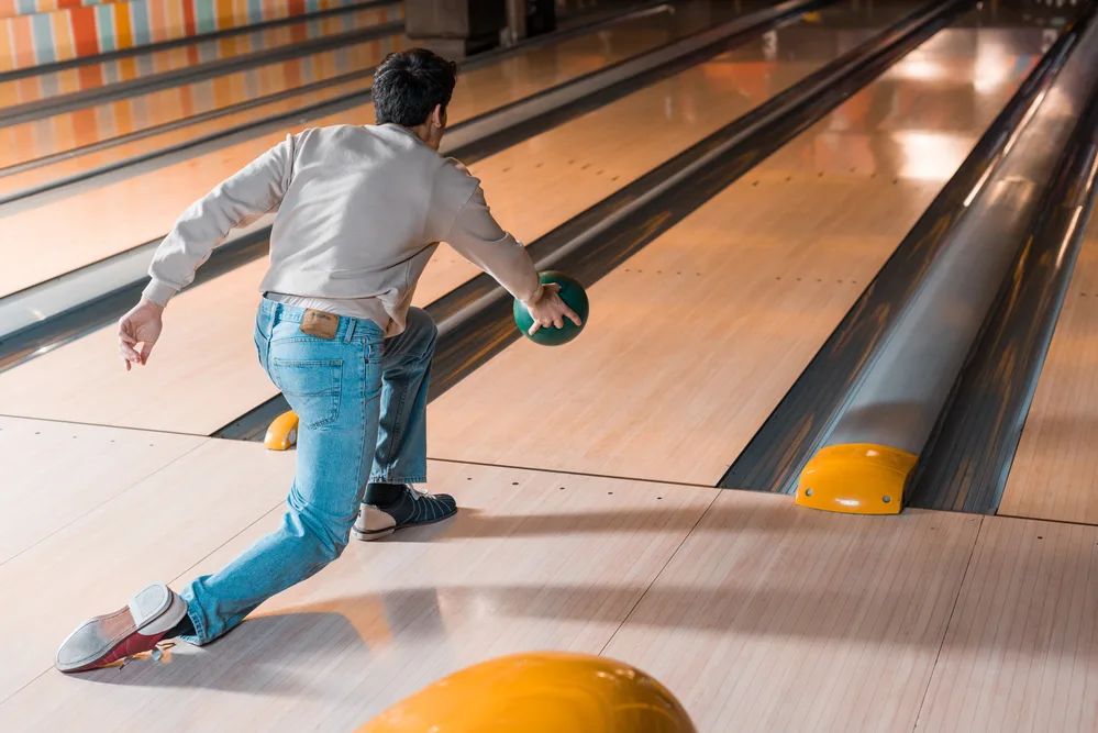 The bowler wearing a typical pair of leather shoes releases the green ball at the foul line.