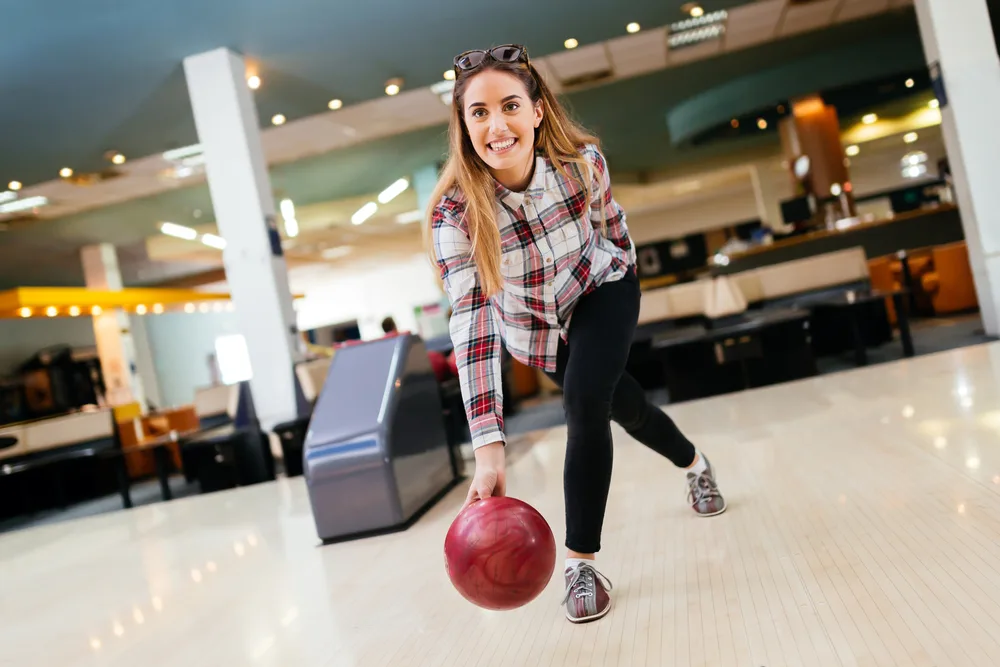 The lady wearing a plaid red and white shirt, with black pants, bowling shoes (street shoes are not allowed) used a single bowling lane to practice for her bowling league.