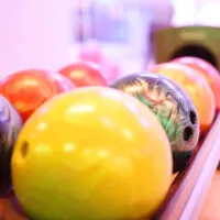 Two rows of multiple bowling balls on a ball return that have perfect ball surface.