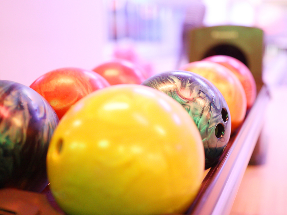 Two rows of multiple bowling balls on a ball return that have perfect ball surface.