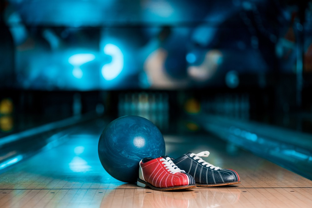 A pair of tri-colored bowling shoes on a lane at the foul, with a blue bowling ball are required, as casual shoes are not permitted.
