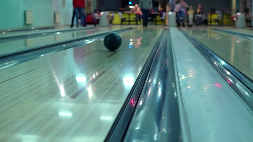 A man throws a bowling ball straight down the lane for a straight shot to win the bowling game.