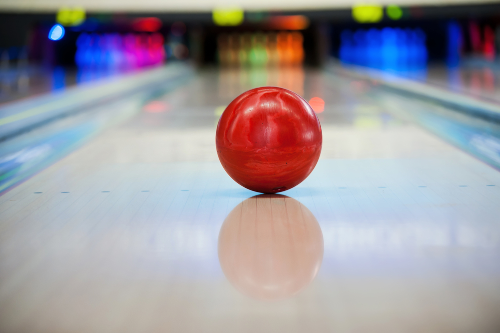 Close-up of bright red bowling ball rolling straight down the bowling alley because house balls do not hook.