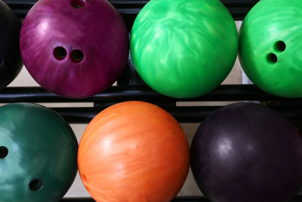 Bowlers can choose the best bowling balls from colorful balls on rack in a bowling alley.