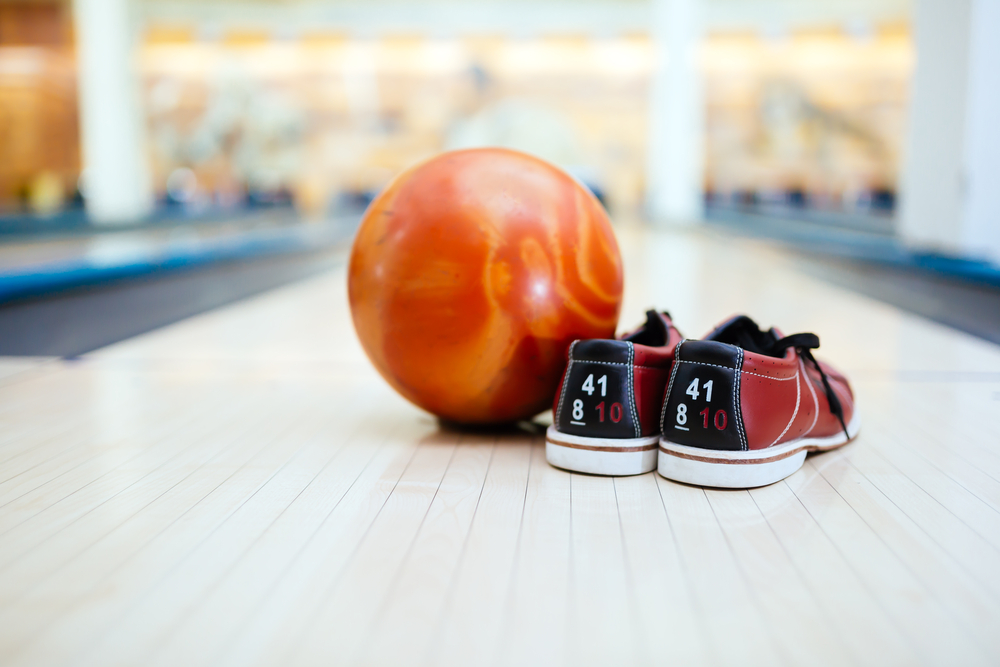 A pair of tri colored, red, blue and white, bowling shoes on a bowling lane at the foul line that has been cleaned with uv light.