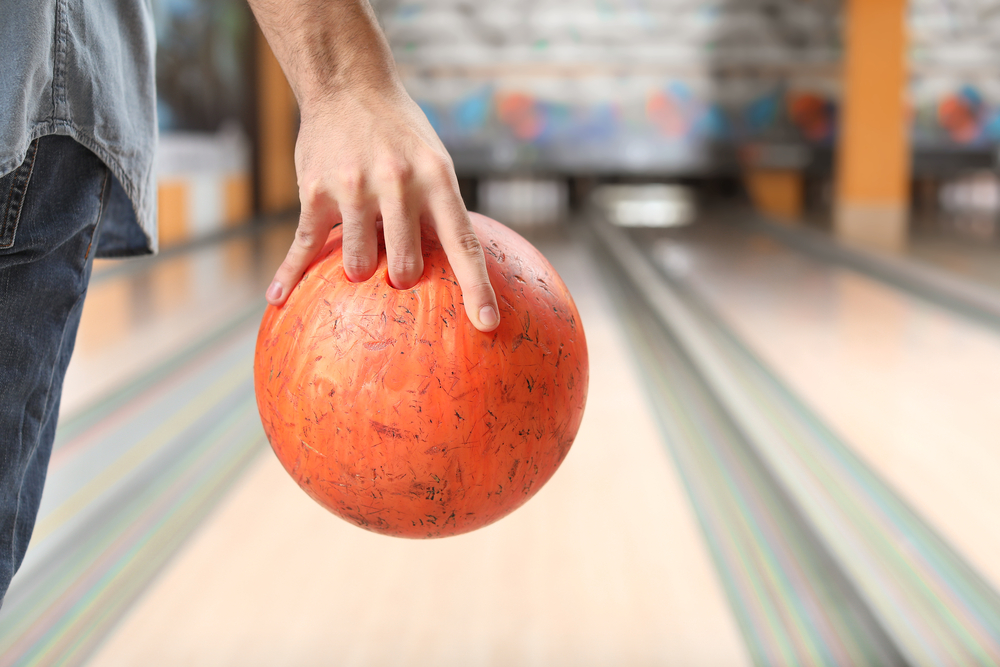 Man holds an orange plastic ball in his bowling hand, that is found at most bowling alleys.