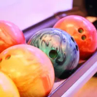 A row of reactive resin bowling balls and plastic bowling balls on the ball return.