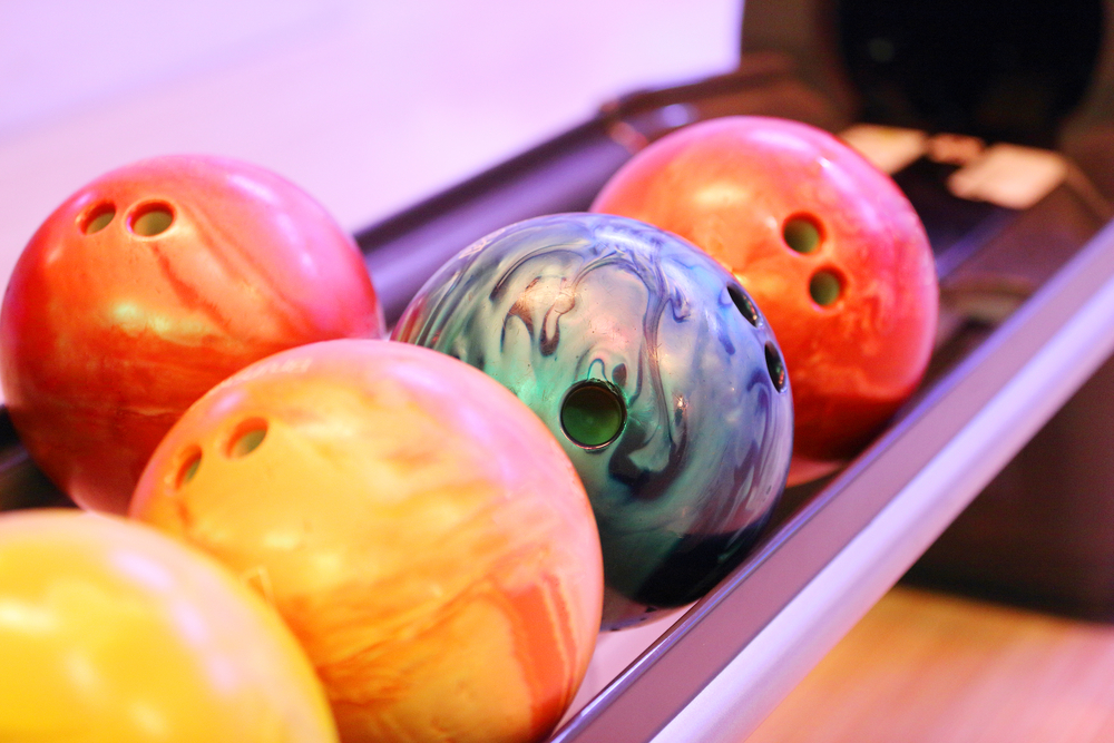 A row of reactive resin bowling balls and plastic bowling balls on the ball return.