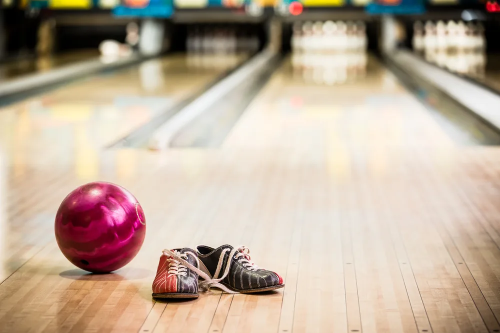 Tri-colored bowling shoes that professional bowlers wear are on a lane with a bowling ball.