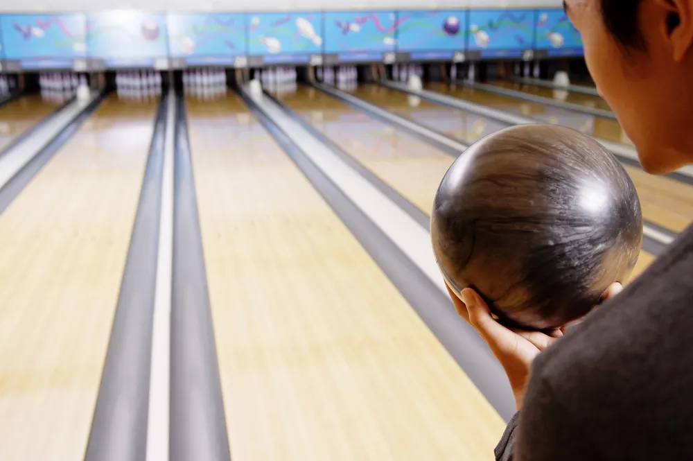 The young man, a  bowling aficionado, stands at the foul line, holding his bowling ball in his in home bowling alley, admiring his lastest diy project.