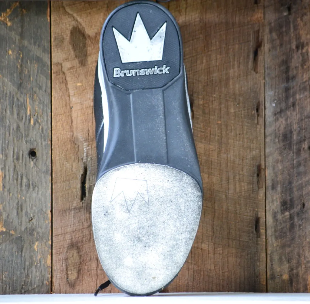 A black and gray brunswick bowling shoes with rubber soles and dirty bowling shoe slides affect the bowlers game. Cleaning the bowling shoes is recommended.