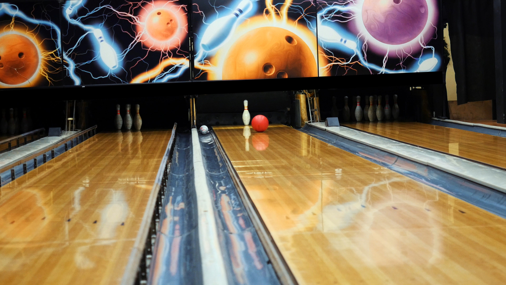 Three bowling lanes appear in the image, and a single pin remains after the left handed bowler failed to clear the split.