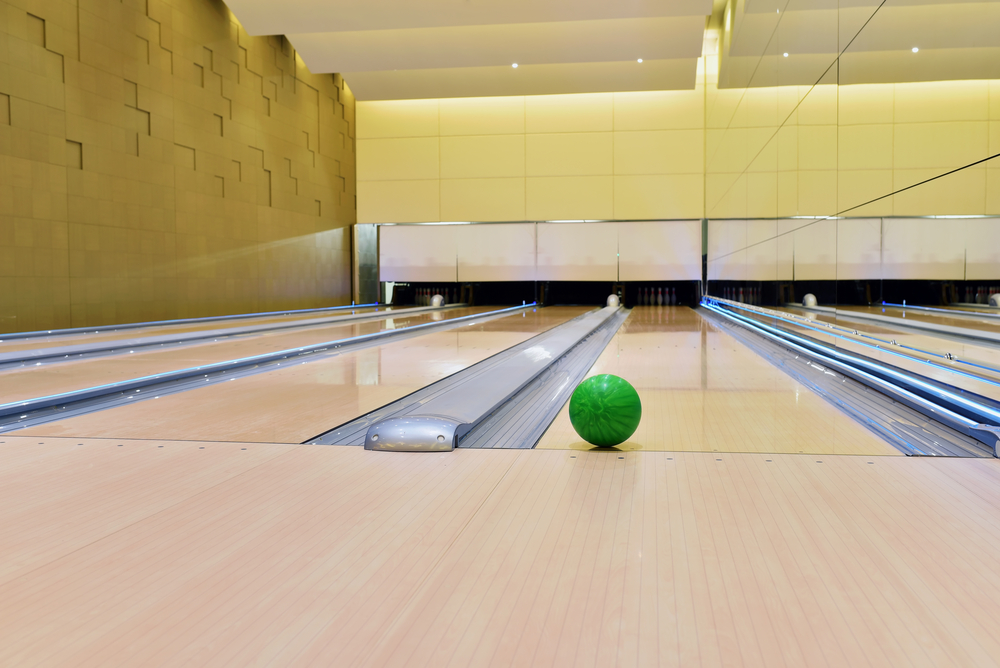 Four lanes are visible, and their gutters are a gray material. A green ball sits just over the foul line in the fourth lane. If the ball lands in the gutter, the bowler receives zero points.