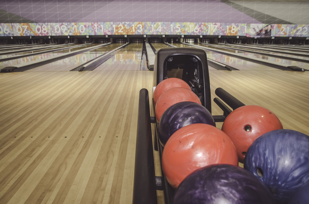 The ball return sits a few feet from the foul and has the red, blue, and purple colored bowling ball on top.