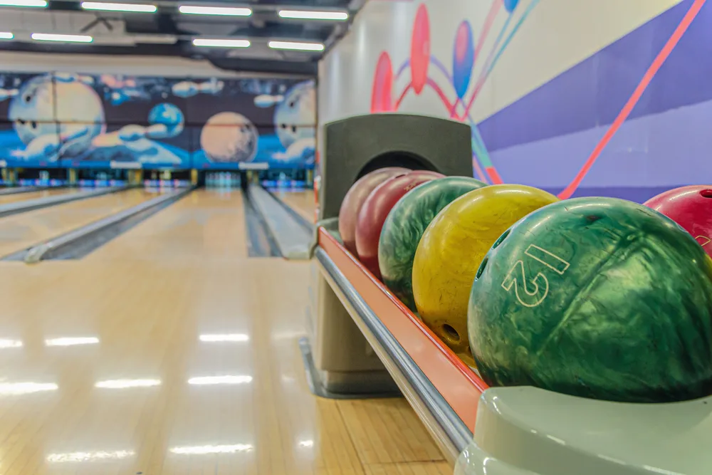 Typical bowling alley lane bowling with bowling ball markings on the wall, visible gutters, foul line, ball return with colorful balls. Bowlers of different skill levels can use this lane from professional bowlers to high school.