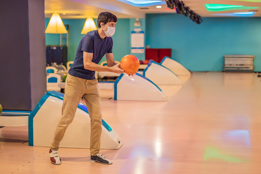 Man playing bowling with an orange house ball, holding the ball in his bowling arm.