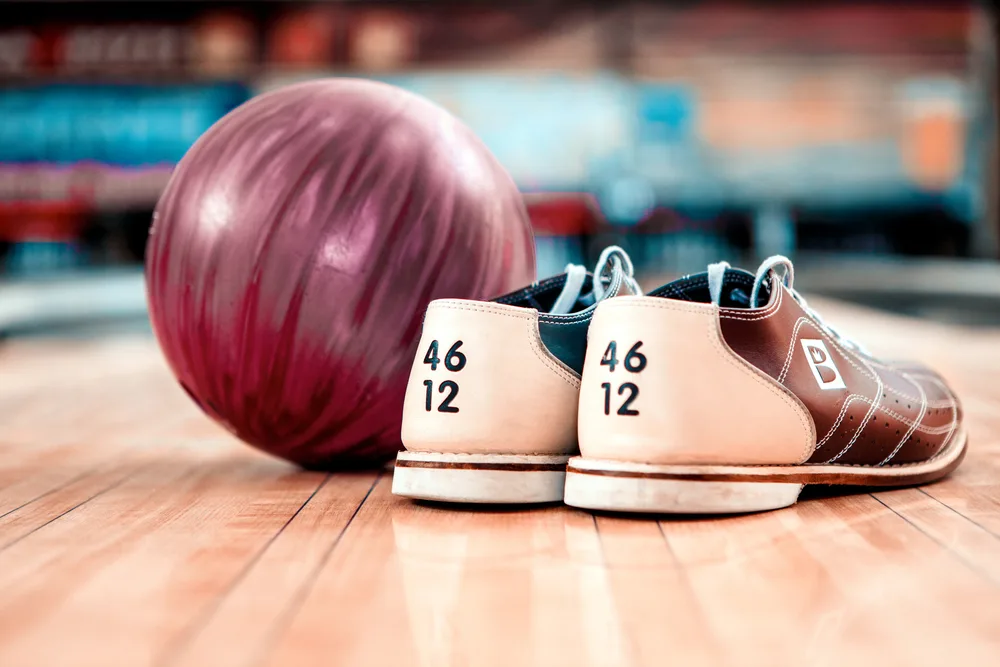 Close up of bowling sliding shoe and lilac ball lying on bowling alley lane where running shoes are not allowed.