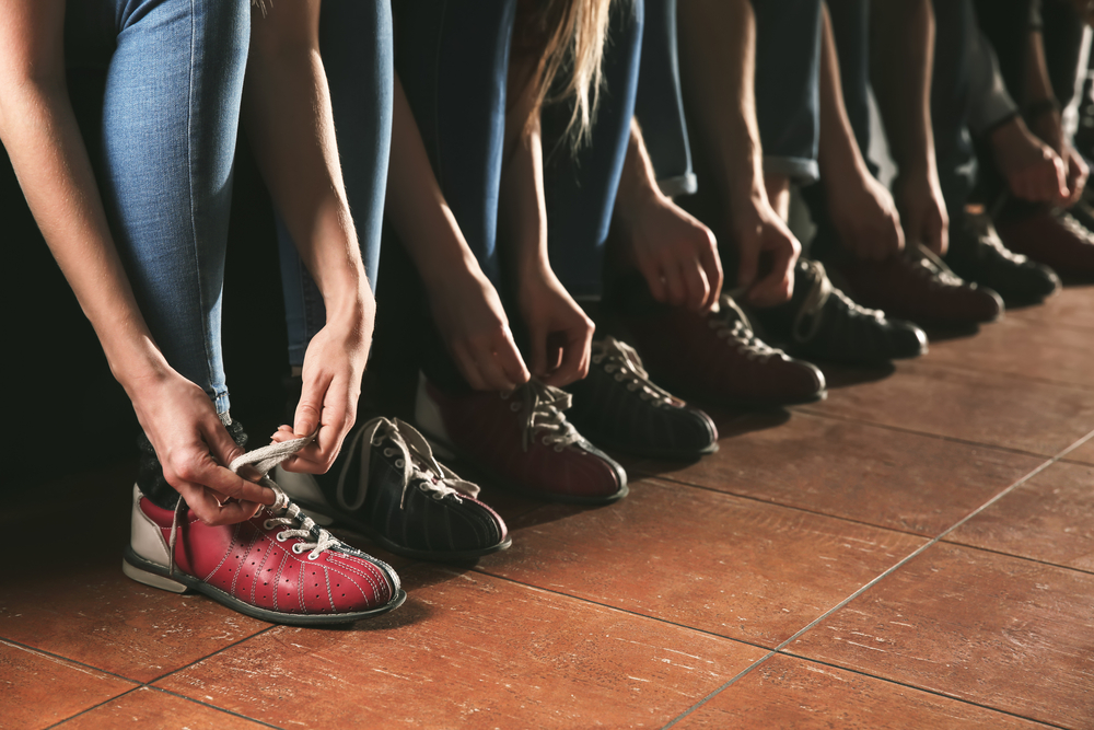 A group of people lacing up their rented bowling shoes. The simplest method to cleaning bowling shoes is with a damp cloth and disinfectant spray.