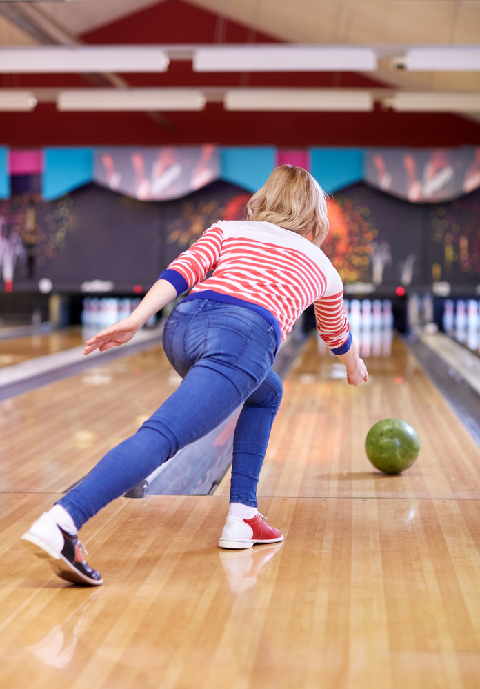 The female bowler release the green bowling ball unto the lane using the technique to curve the bowling ball into the pocket.