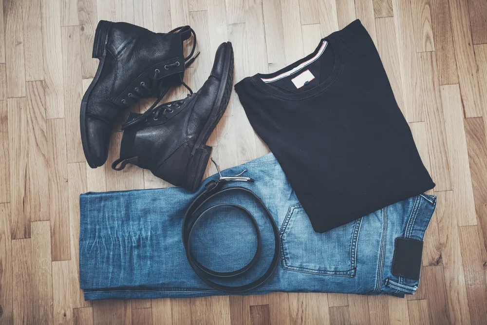 Black t-shirt, blue denim pants with black belt, and black boots on a brown wooden background. You can wear them to a fancy restaurant on your first date.