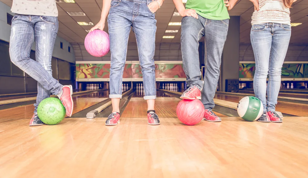 Four people standing on a lane all with their own colorful bowling ball.