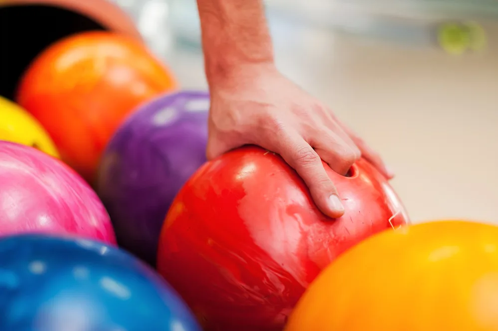 Multi-colored bowling balls sit on the ball return as the professional bowler chooses the red and heaviest bowling ball for their arsenal for the strike.