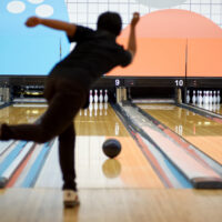 A young man throwing a ball straight in front of a ten-pin alley; this is called straight bowling.