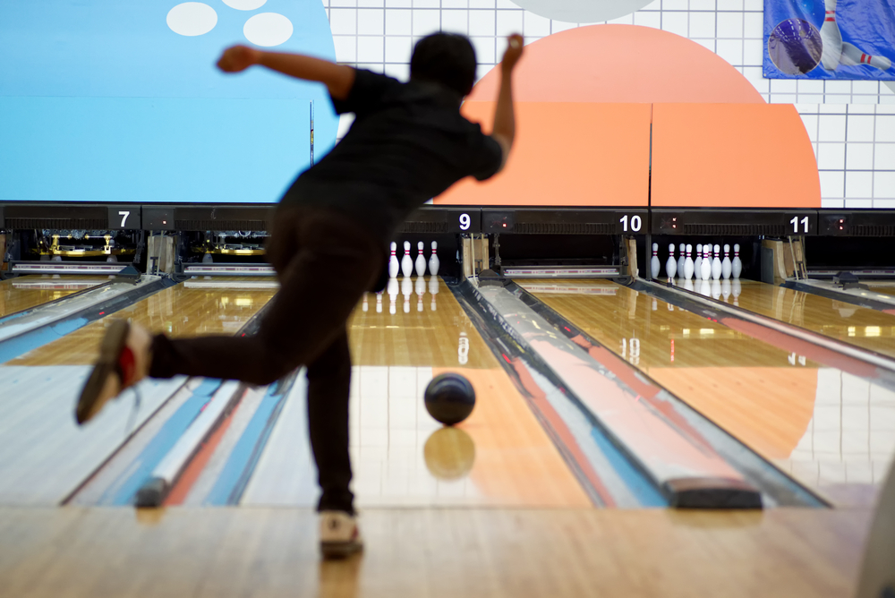 A young man throwing a ball straight in front of a ten-pin alley; this is called straight bowling.