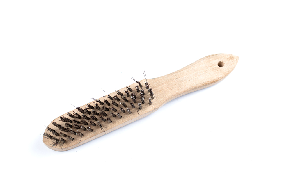 A wire bristled brush or steel wire brush on a white background is used to brush the felt bottom of bowling shoes that affects the bowler's glide.