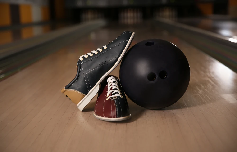 Tri-colored blue, burgundy and tan bowling shoes and with a reactive resin ball on the bowling lane in a club.