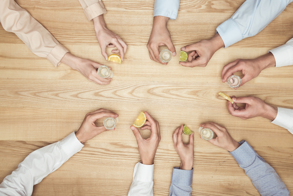Five friends holding shot glasses in their right hand and a slice of lemon or lime in their left hands for a bowling drinking game they are to avoid over consumption of alcohol.